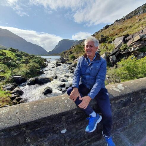 Guest enjoying scenic river view at mountain retreat with lush greenery and rocky landscape.
