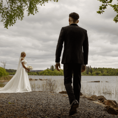 Picturesque lakeside wedding scene with bride and groom, lush green surroundings, serene water view, romantic moment.