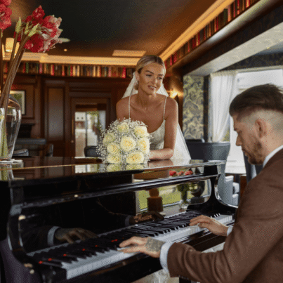 Elegant couple in hotel piano lounge, enjoying romantic music with vibrant flowers, cosy decor, and scenic views.