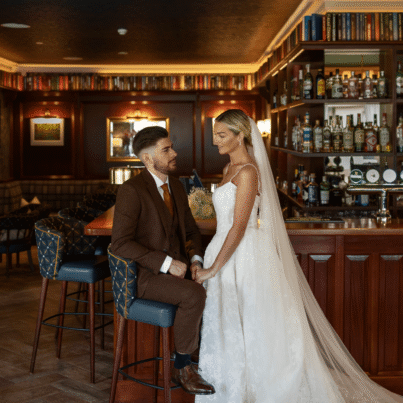 Elegant couple enjoying cosy hotel bar with rich wooden decor and curated drinks, ideal for weddings and romantic getaways.