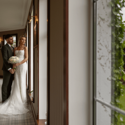 Couple admires garden view through elegant hotel windows, highlighting wedding venue with lush green scenery and classic decor.