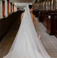 Elegant bride in white gown walking down a luxurious hotel corridor with wood panelling and framed artwork.
