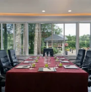 Spacious conference room with large windows facing lush garden, comfy chairs, and elegant table setup in luxury hotel.