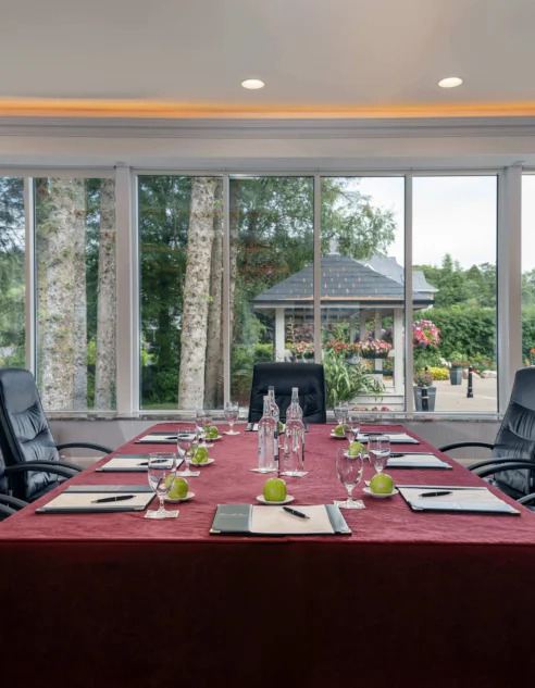 Spacious conference room with large windows facing lush garden, comfy chairs, and elegant table setup in luxury hotel.