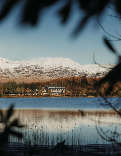 Lakeside hotel with waterfront views, snow-capped mountains, woodland and calm reflection — peaceful luxury retreat with scenic vistas